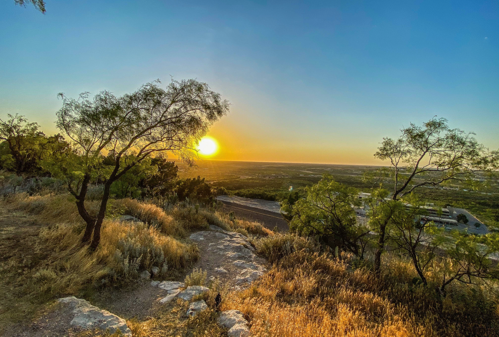 A  rising sun bathes in the landscape in a golden hue with the rugged terrain of a brightening sky.