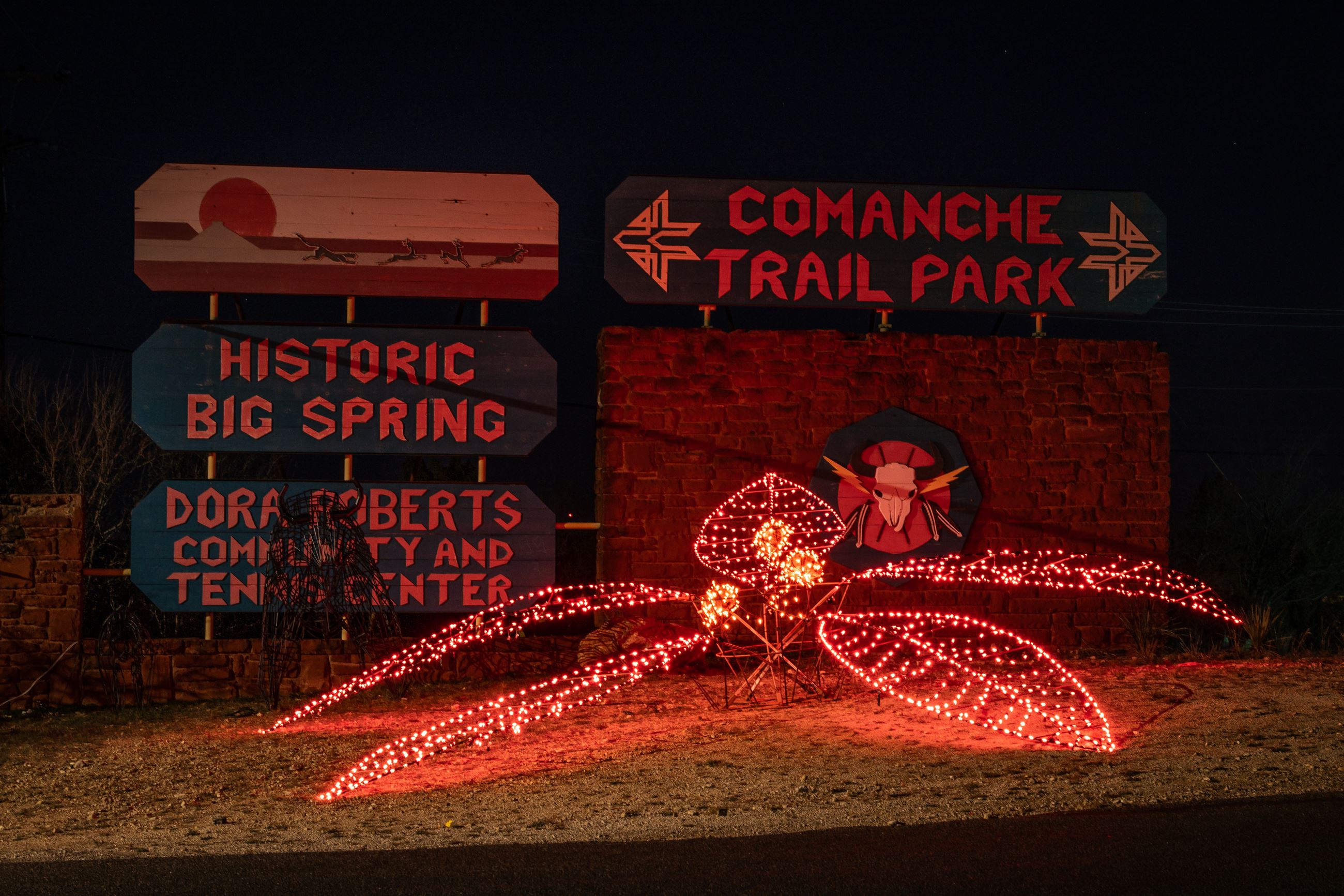 A lighted poinsettia displayed next to the Comanche Trail Park entrance sign. 